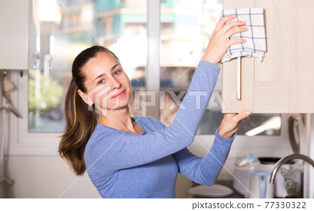 Smiling woman is cleaning surface on the kitchen at the home 77330322