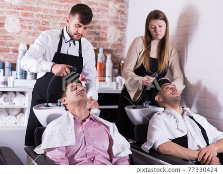 Men relaxing while hairdressers washing their hair 77330424