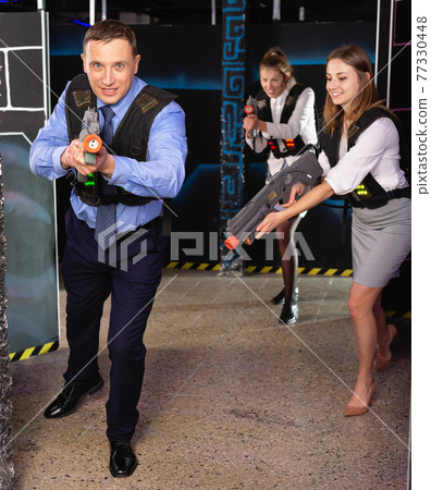 Men and women in business suits playing laser tag emotionally in dark room Men and women in business suits playing laser tag emotionally in dark room 77330448