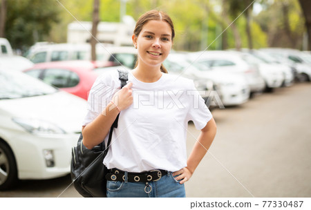 Portrait of a positive girl standing on the street near cars Portrait of a positive girl standing on the street near cars 77330487
