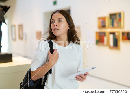 Girl visitor examines an exhibit standing in an art gallery 77330820