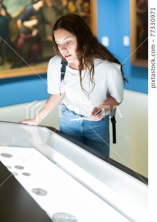 Attentive girl visitor at the museum looks at the exposition behind a glass display case 77330971
