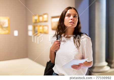 Thoughtful young girl in an art gallery studies works of art 77330992
