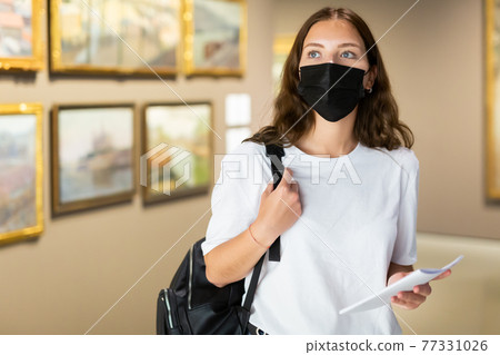 Young girl in a protective mask visits an exhibition of paintings in a museum 77331026