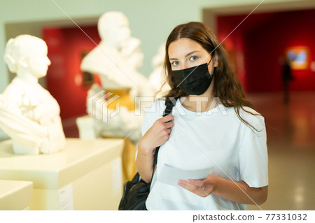 Young girl wearing a protective mask in the museum examines the bust 77331032