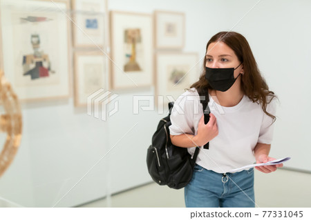Interested girl in a protective mask in the art gallery studies the works of art Interested girl in a protective mask in the art gallery studies the works of art 77331045