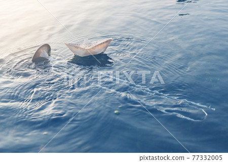 wind instrument pipe lies in the water, in the sea or ocean, next to a paper boat of music, a concept wind instrument pipe lies in the water, in the sea or ocean, next to a paper boat of music, a concept 77332005