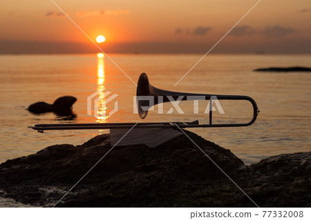 wind instrument pipe lies near the sea on a stone on the background of the red dawn 77332008