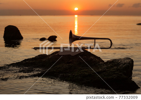 wind instrument pipe lies near the sea on a stone on the background of the red dawn 77332009