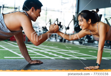 Healthy smiling couple of man and woman giving high five to each other while pushing up in the fitness gym. Asian sporty people working out together Healthy smiling couple of man and woman giving high five to each other while pushing up in the fitness gym. Asian sporty people working out together 77333156