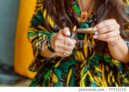 A stick of Palo Santo tree in the hands of a girl. A woman lights a stick. Close up. 77333218