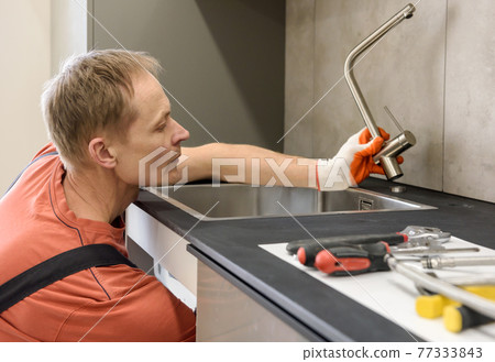 The plumber is installing a faucet on the kitchen sink. The plumber is installing a faucet on the kitchen sink. 77333843