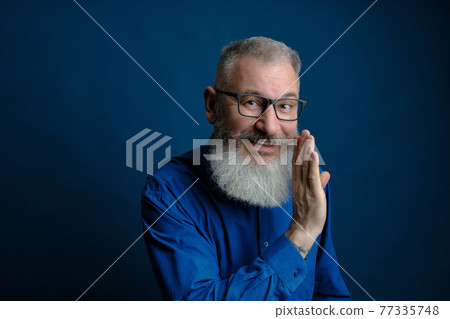 Bearded middle age man dressed blue shirt holds hand near mouth, secret talk concept, blue background 77335748