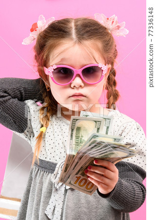 Little girl in glasses with a package and money on a pink background, child and shopping. Little girl in glasses with a package and money on a pink background, child and shopping. 77336148