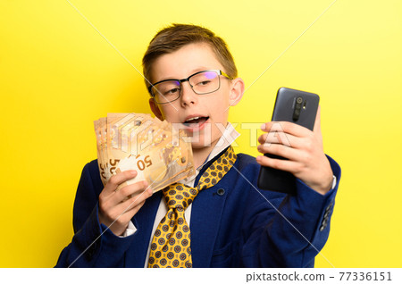 Boy in a big suit, selfie on a yellow background with money. Boy in a big suit, selfie on a yellow background with money. 77336151