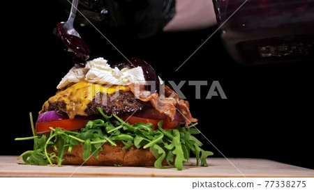 Craft burger is cooking on black background. Consist: sauce, arugula, tomato, onion, bacon, currant sauce, ricotta cheese, air bun and marble meat. Craft burger is cooking on black background. Consist: sauce, arugula, tomato, onion, bacon, currant sauce, ricotta cheese, air bun and marble meat. 77338275