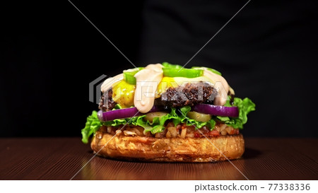 Craft burger is cooking on black background. Consist: sauce salsa, lettuce, red onion, pickle, cheese, chilli green pepper, bun, marbled meat beef. Craft burger is cooking on black background. Consist: sauce salsa, lettuce, red onion, pickle, cheese, chilli green pepper, bun, marbled meat beef. 77338336