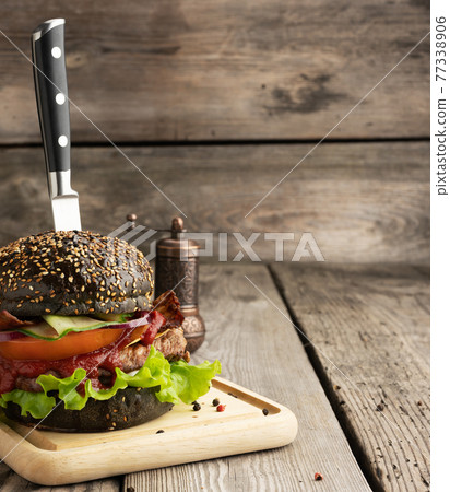 cheeseburger with black bun, meat and vegetables on a wooden background, cheeseburger with black bun, meat and vegetables on a wooden background, 77338906