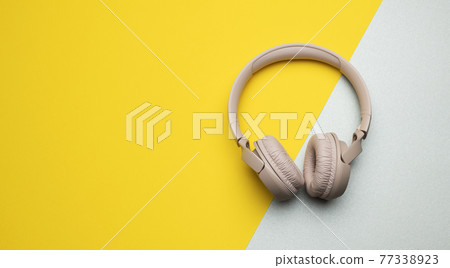 pink wireless headphones on a gray-yellow background, top view. Modern gadget 77338923
