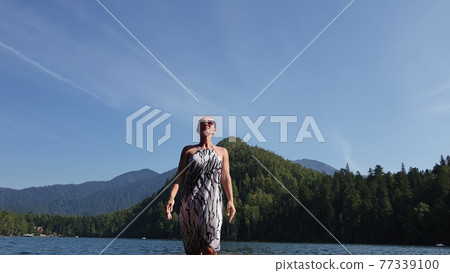 Woman walk on water on pier in sunglasses and a boho silk shawl. Girl rest on flood wood underwater dock. The pavement is covered with water in lake. Woman walk on water on pier in sunglasses and a boho silk shawl. Girl rest on flood wood underwater dock. The pavement is covered with water in lake. 77339100
