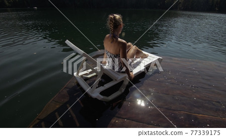 Woman lie on a sunbed in sunglasses and a boho silk shawl. Girl rest on a flood wood underwater pier. The pavement is covered with water in the lake. Woman lie on a sunbed in sunglasses and a boho silk shawl. Girl rest on a flood wood underwater pier. The pavement is covered with water in the lake. 77339175