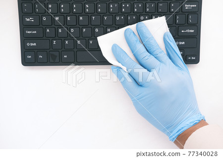 hand in blue rubber gloves and white tissue disinfecting keyboard  77340028