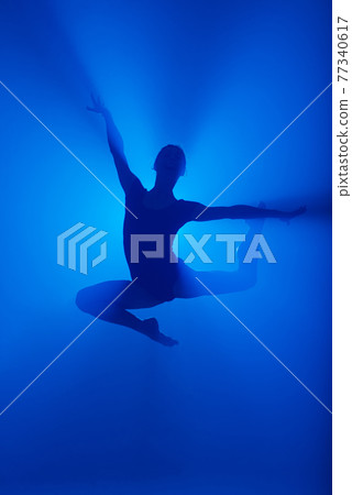 Professional ballerina dancing ballet in smoke. Female in black bodysuit on floodlights background. Professional ballerina dancing ballet in smoke. Female in black bodysuit on floodlights background. 77340617