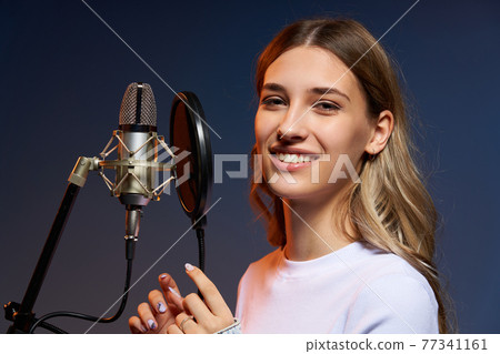 Closeup portrait of young Caucasian girl with microphone and pop-up filter looking at camera Closeup portrait of young Caucasian girl with microphone and pop-up filter looking at camera 77341161