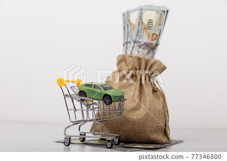 Model of car in shopping cart with money bag on white background Model of car in shopping cart with money bag on white background 77346800