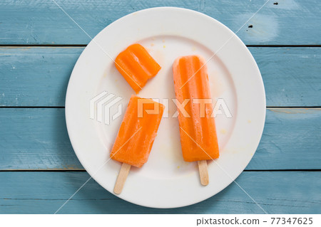 Orange popsicles on blue wooden background Orange popsicles on blue wooden background 77347625