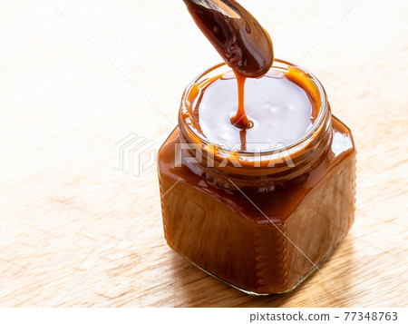 cooking salted butter caramel sauce at home kitchen - homemade smooth salty caramel dessert in open glass jar on wooden board close up cooking salted butter caramel sauce at home kitchen - homemade smooth salty caramel dessert in open glass jar on wooden board close up 77348763