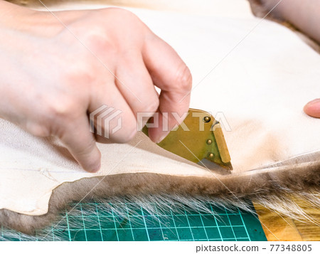master cuts the edge of fur pelt by knife 77348805