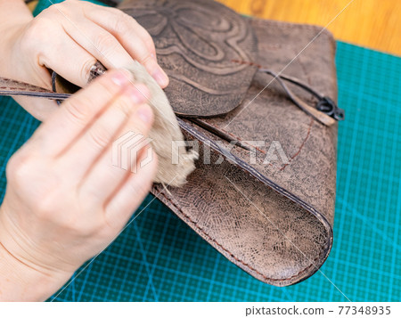 craftsman polishes the handbag with wax 77348935