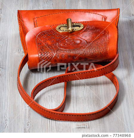 orange colored embossed leather bag on gray table 77348968