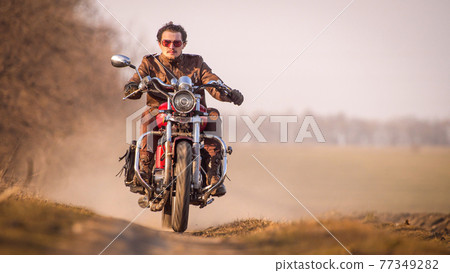 Young curly biker with red glasses drive ride on red chopper 77349282