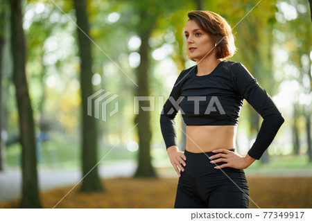 Woman in activewear relaxing between exercises at park 77349917