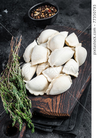 Frozen raw dumplings pierogi with potato on a wooden board. Black background. Top View Frozen raw dumplings pierogi with potato on a wooden board. Black background. Top View 77350793