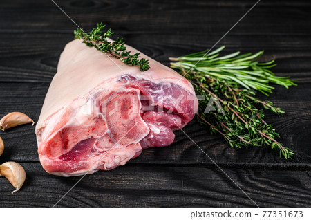 Raw Pork knuckle leg meat on kitchen table with herbs. Black wooden background. Top view 77351673