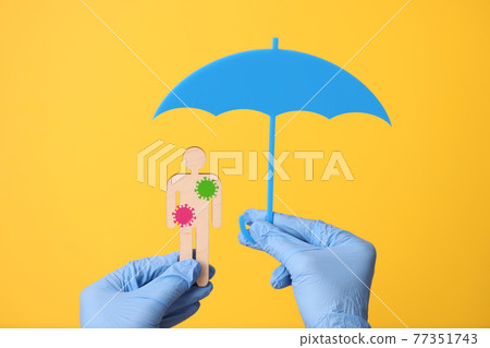 Hands in gloves hold wooden man with stickers bacteria and an umbrella Hands in gloves hold wooden man with stickers bacteria and an umbrella 77351743