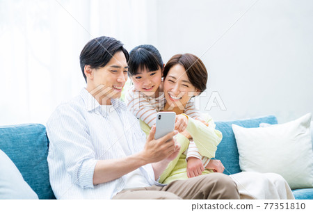 A close family looking at a smartphone in the living room 77351810