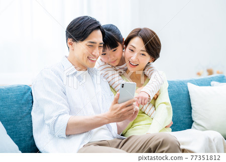 A close family looking at a smartphone in the living room 77351812