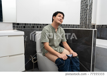 happy man sitting in toilet bowl in bathroom at home happy man sitting in toilet bowl in bathroom at home 77355333