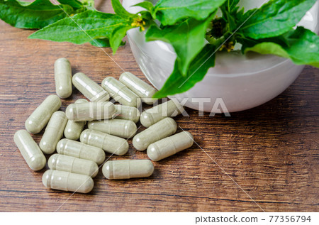 Pile of herbal medicine in capsules and ceramic mortar with green leaf. 77356794