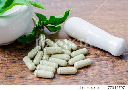 Pile of herbal medicine in capsules and ceramic mortar with green leaf. Pile of herbal medicine in capsules and ceramic mortar with green leaf. 77356797