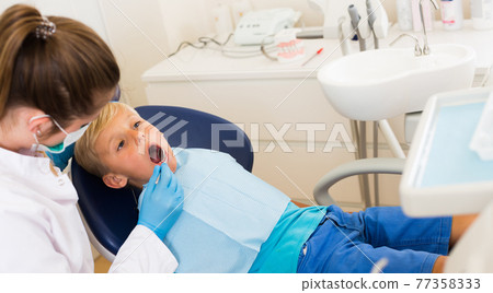 Adult doctor in uniform is taking visional inspection of a teenage Adult doctor in uniform is taking visional inspection of a teenage 77358333