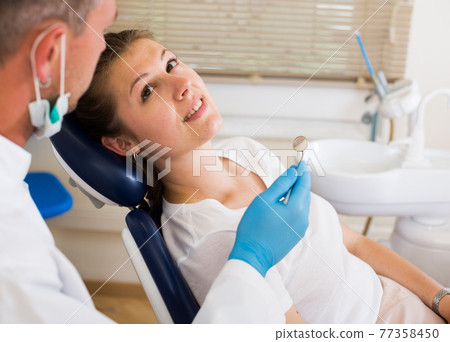 Young doctor in uniform is taking visional inspection of an adult patient on the chair 77358450