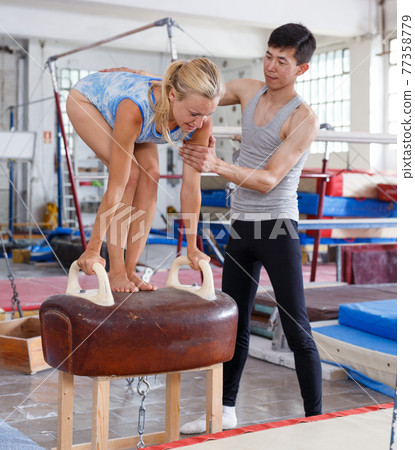 Female gymnast in bodysuit during workout at vaulting buck and man helping 77358779