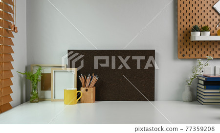 Home office desk with empty frame, pencil holder, coffee cup and houseplant. 77359208