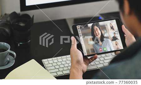 Photo of smart man talking/explaining and sitting in front his computer monitor while video calling with colleague. Working from home through video conference concept. Photo of smart man talking/explaining and sitting in front his computer monitor while video calling with colleague. Working from home through video conference concept. 77360035