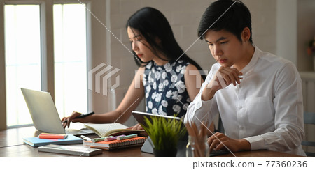 Photo of young office worker working at home. Business couple sitting together at the wooden working desk over comfortable living room as background. 77360236